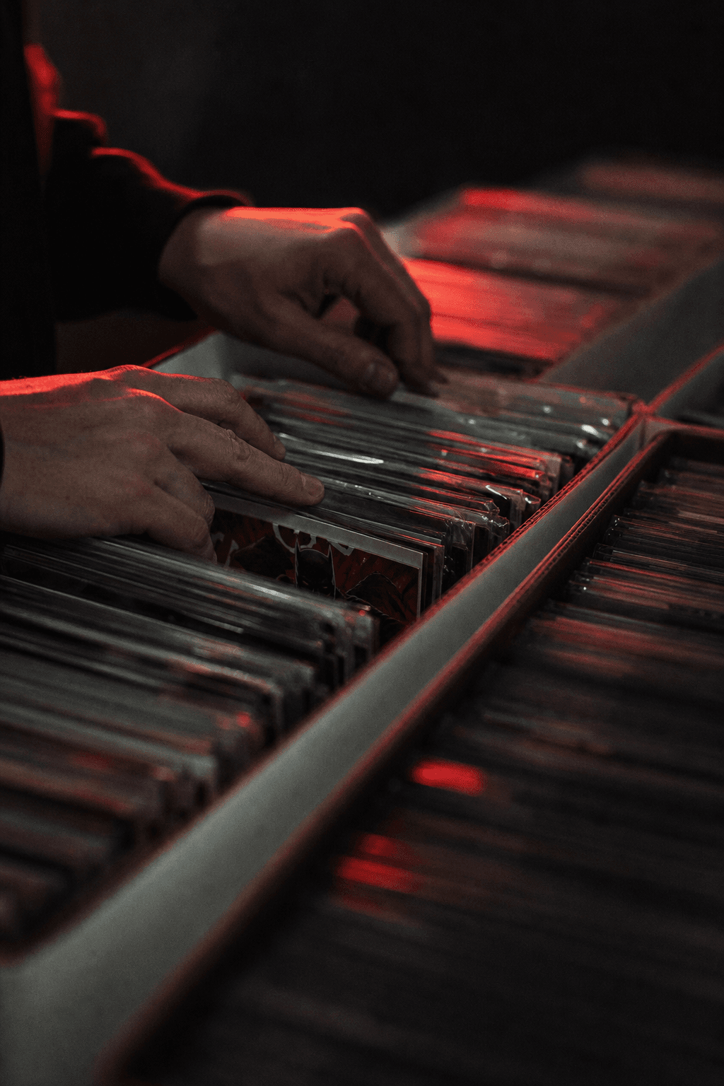 Hands flipping through bagged back issues in a longbox under red light